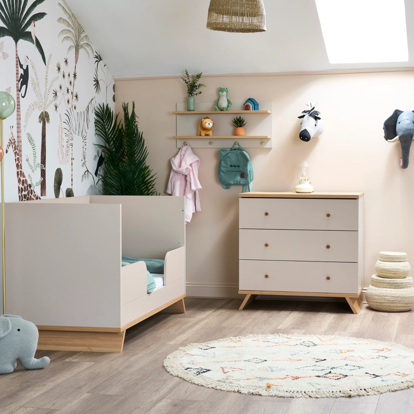 Obaby nursery wall shelf with hooks holding toys and clothes above white chest of drawers in baby room