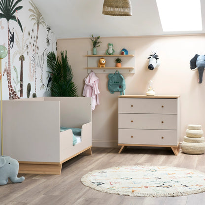 Obaby nursery wall shelf with hooks holding toys and clothes above white chest of drawers in baby room